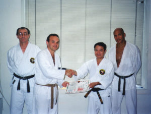 Sensei Troup receives his black belt from Soke Takaoshi Nagamine, with Senseis Crevani (left) and Masters (right).