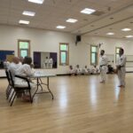 Two karate students prepare to be tested by a table of instructors