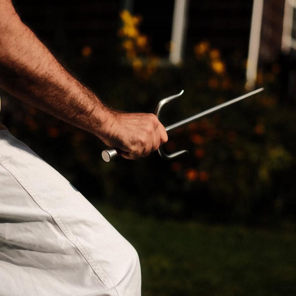 A right hand is visible holding a traditional kobudo sai