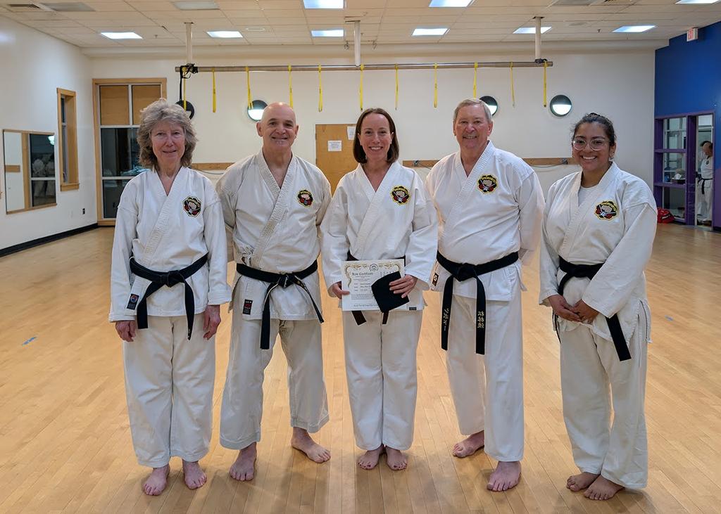 Five karate students pose for the camera, with four black belts surrounding a recently promoted black tip student.