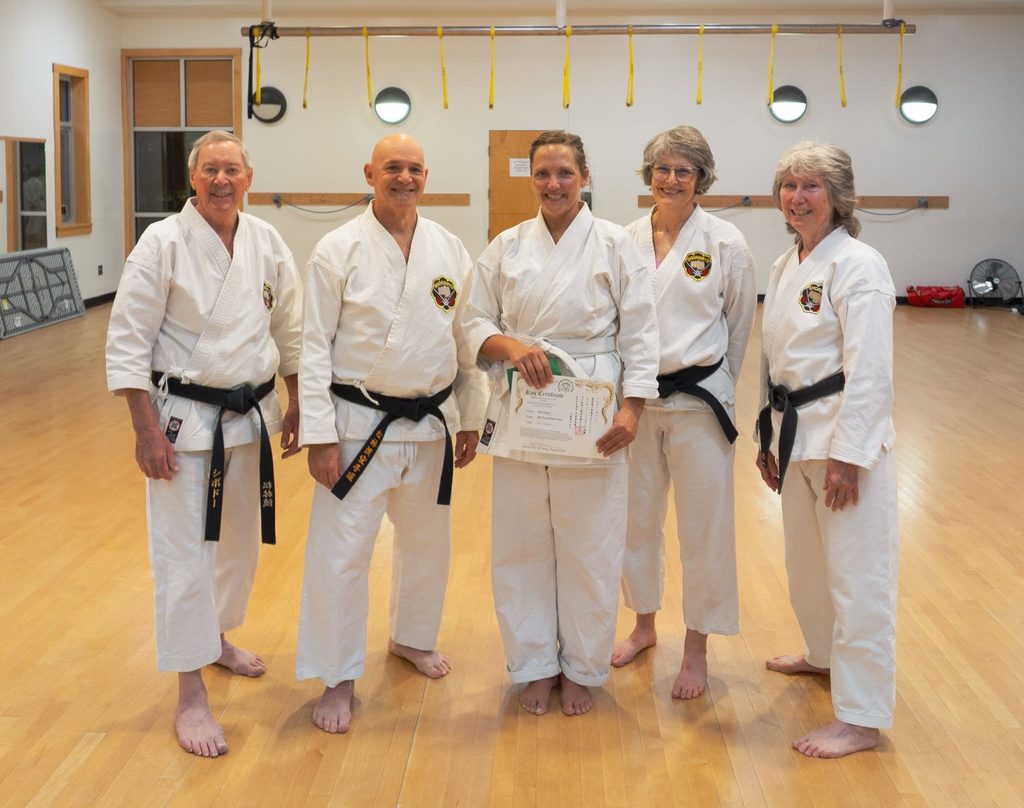 Siiri Soucy stands in the middle of four black belt karate students holding her certificate and her green tips